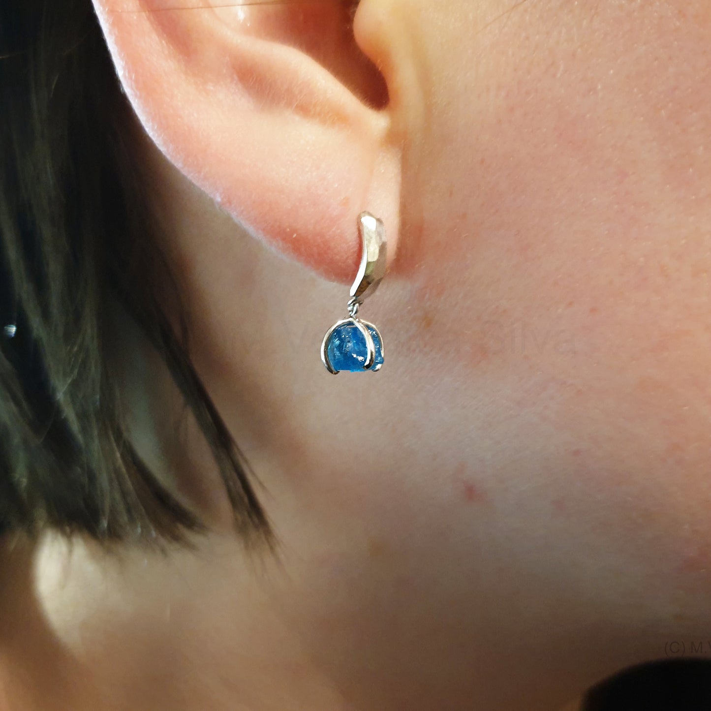 Neon blue apatite, textured silver studs worn on an ear